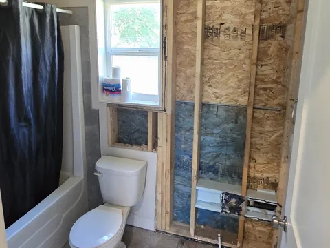 Before: Bathroom wall stripped to the studs and sheathing beside the toilet and window